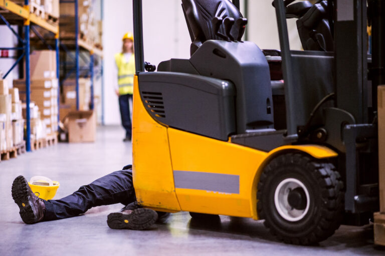 An accident in a warehouse. Woman running towards her colleague lying on the floor next to a forklift.